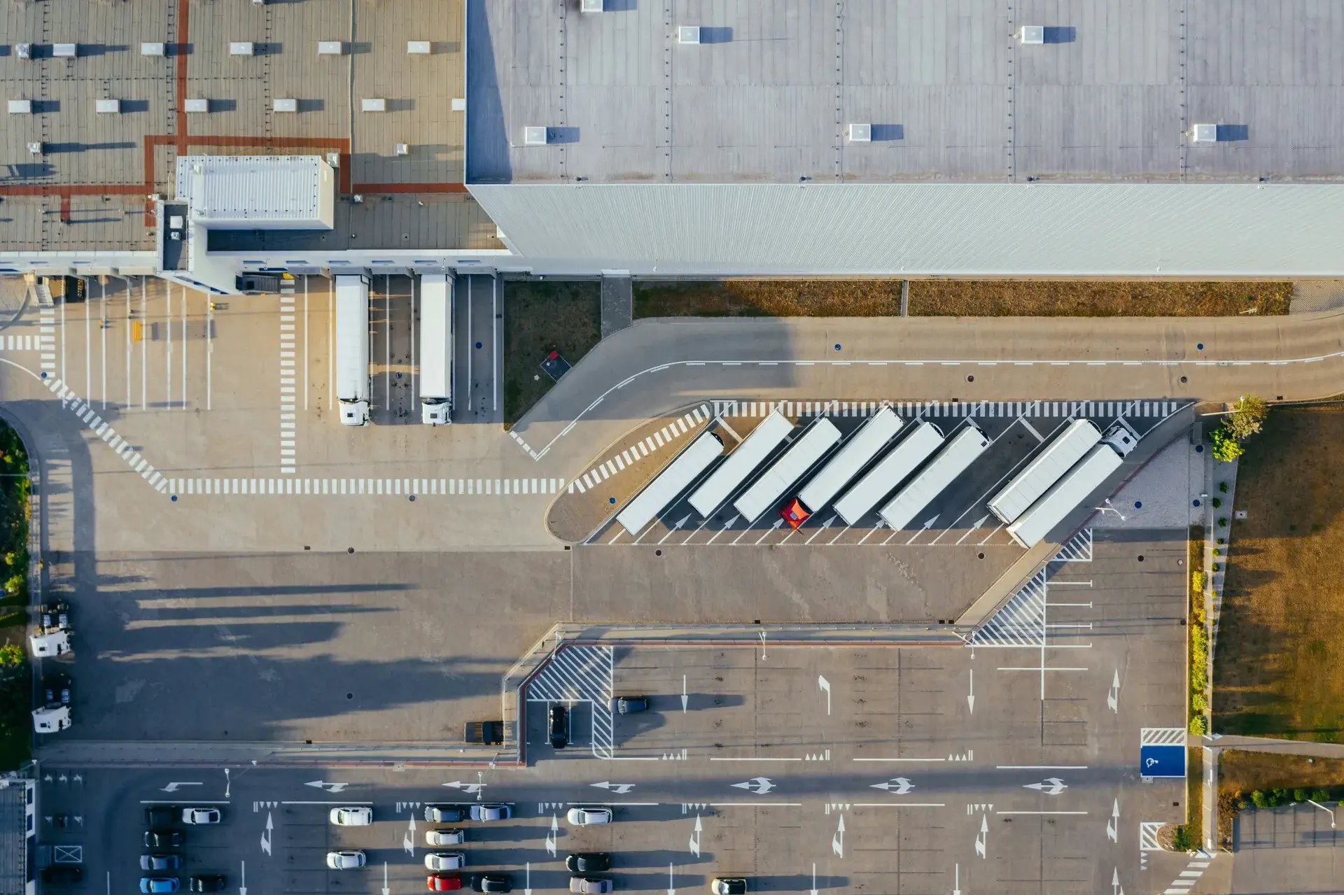 Aerial top-down view of a distribution center with semi-trucks parked at loading docks and cars in the lot.