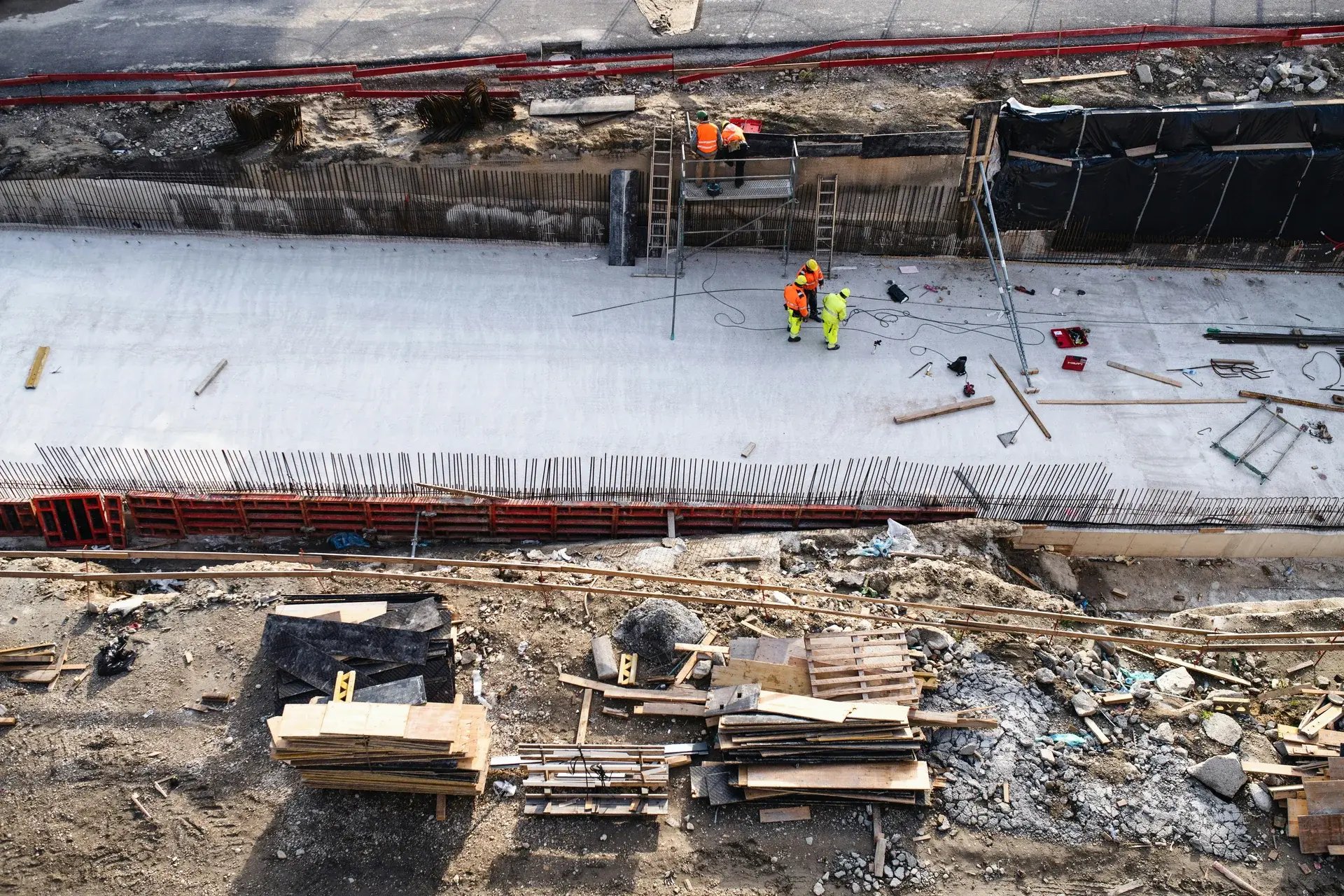 Aerial view of an infrastructure construction site with workers placing rebar and pouring concrete.