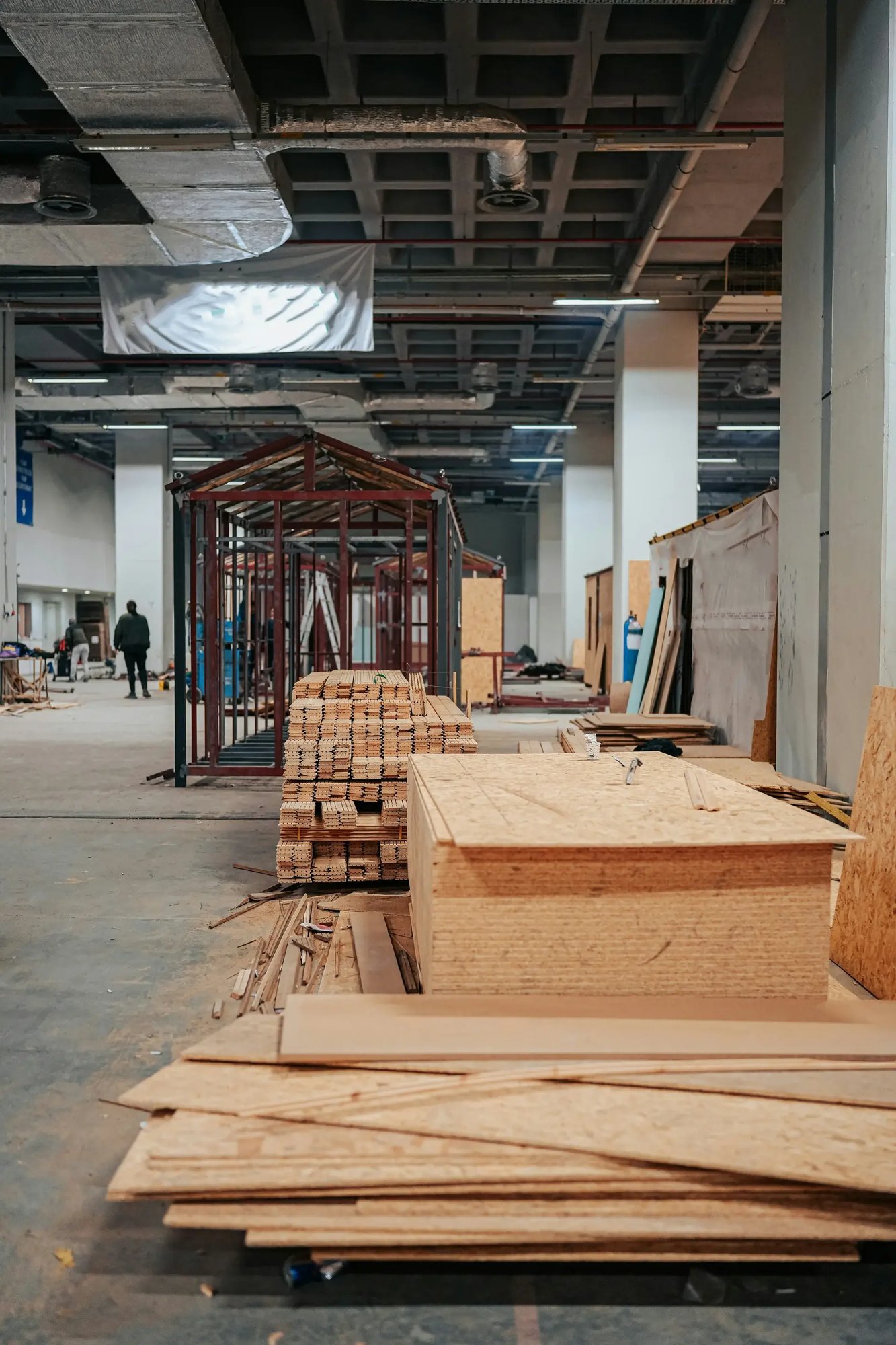 Interior commercial construction buildout with stacks of lumber, plywood sheets, and steel framing in progress.