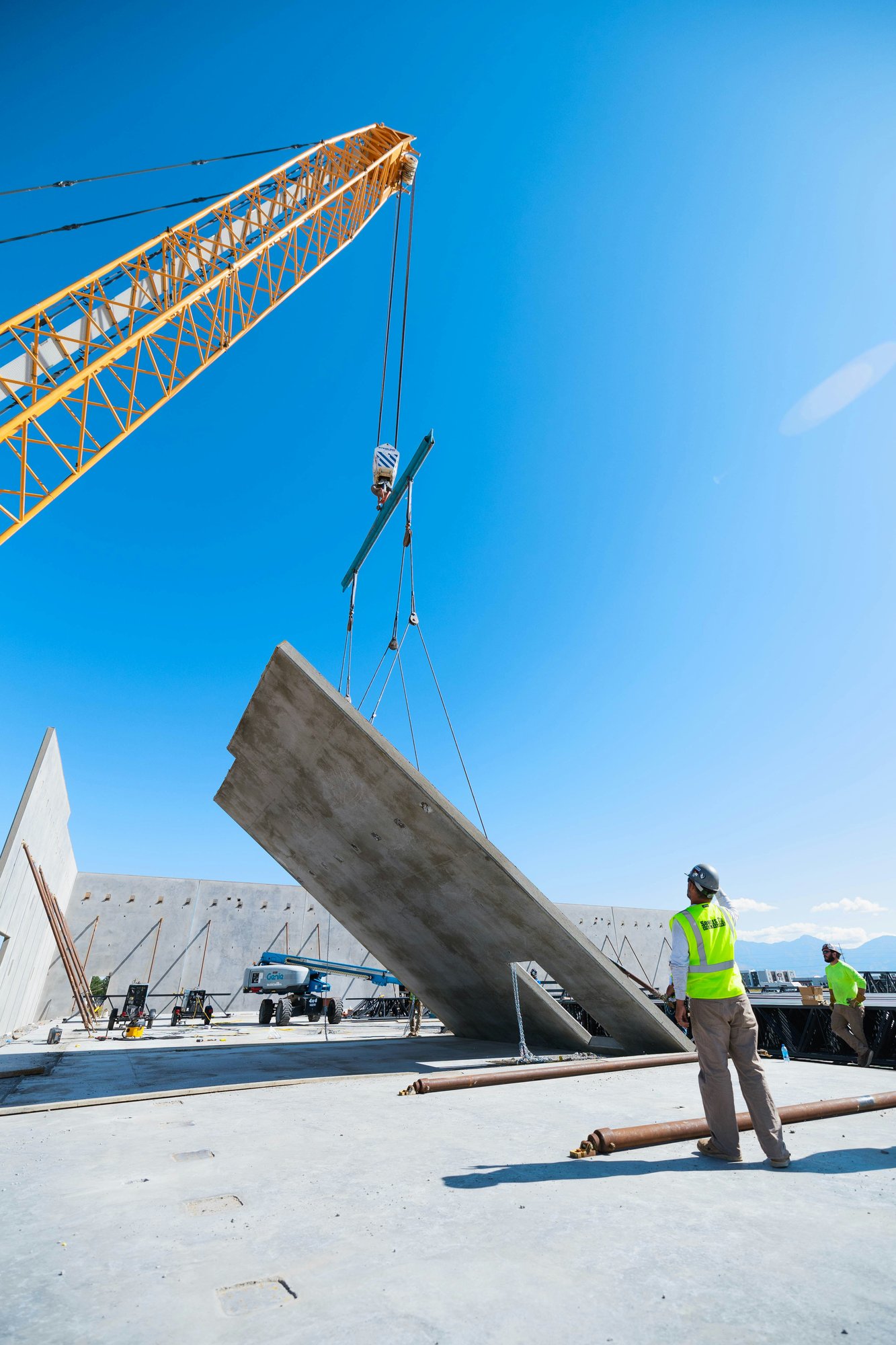 Construction worker signaling as a crane lifts a tilt-up concrete wall panel into position on a commercial jobsite.