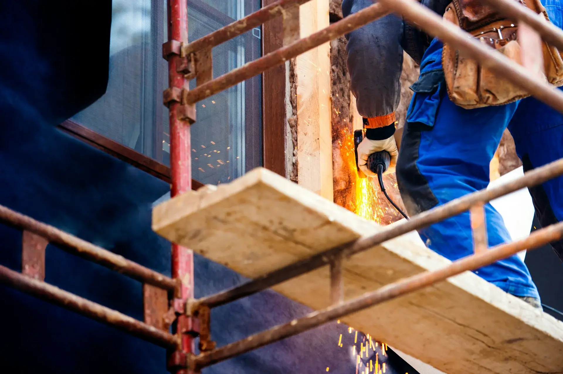 Construction worker using an angle grinder on a metal frame from scaffolding at a building site.
