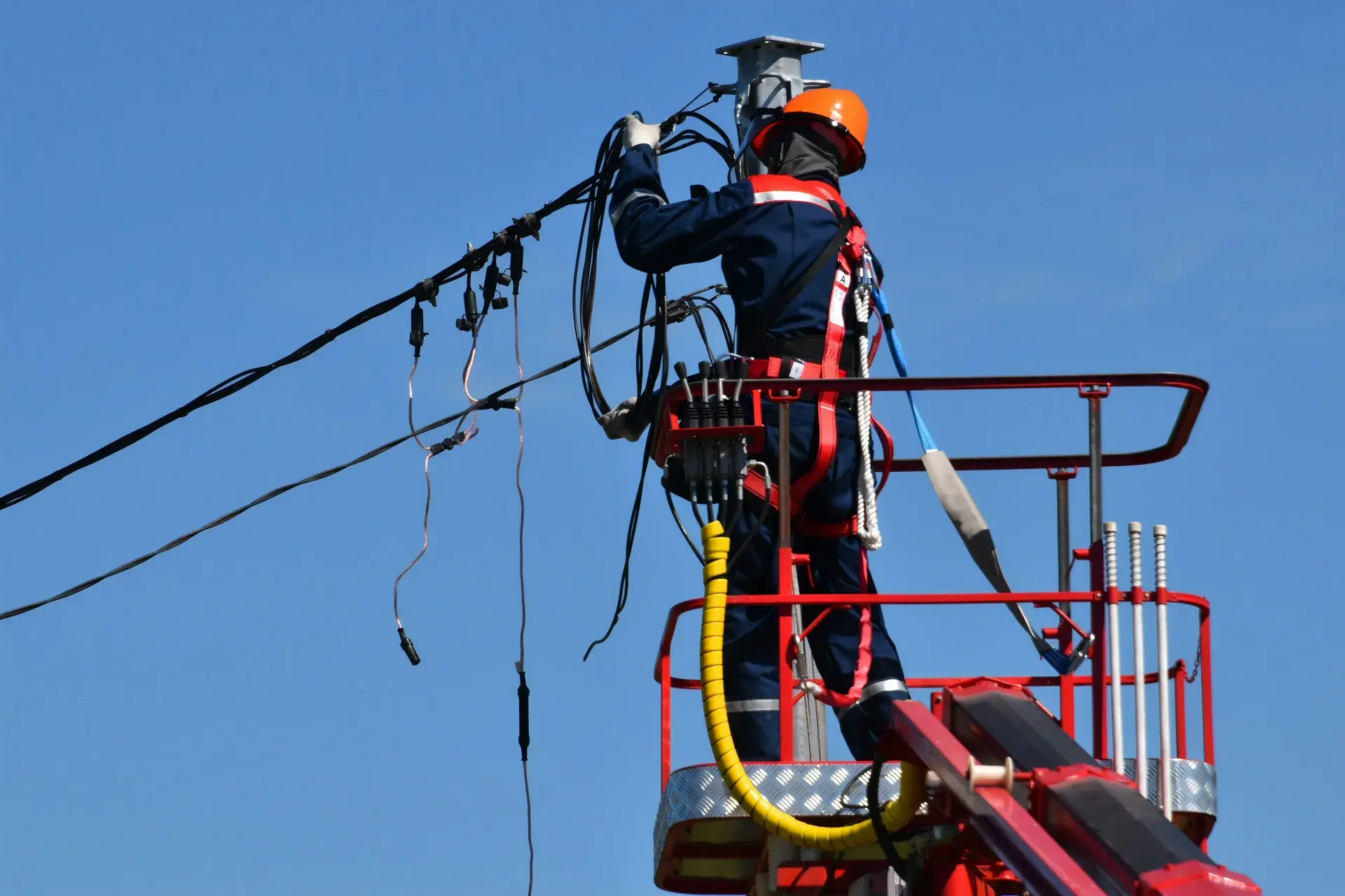 Electrical utility worker in a bucket lift performing maintenance on overhead distribution power lines.