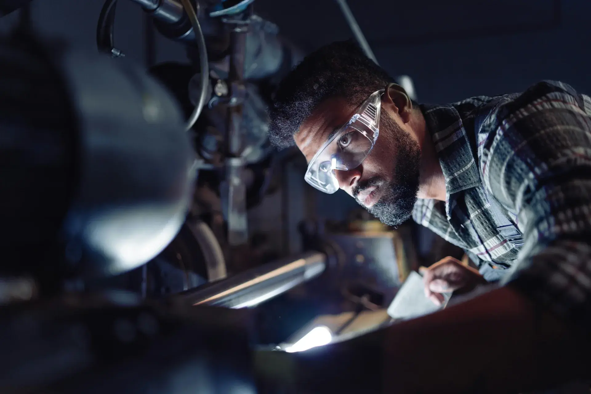 Engineer wearing safety glasses closely inspecting precision industrial machinery in a workshop.