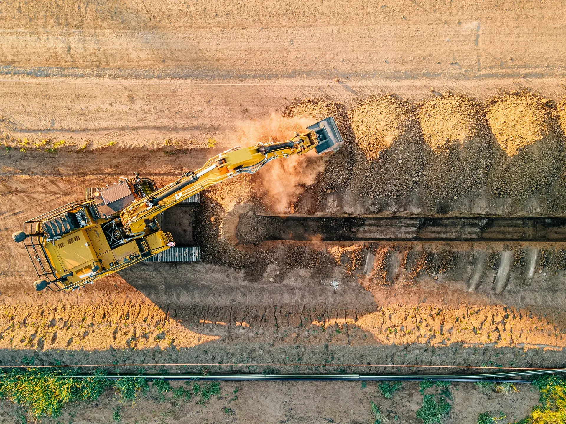 Aerial view of an excavator trenching a long channel for underground utility line installation.