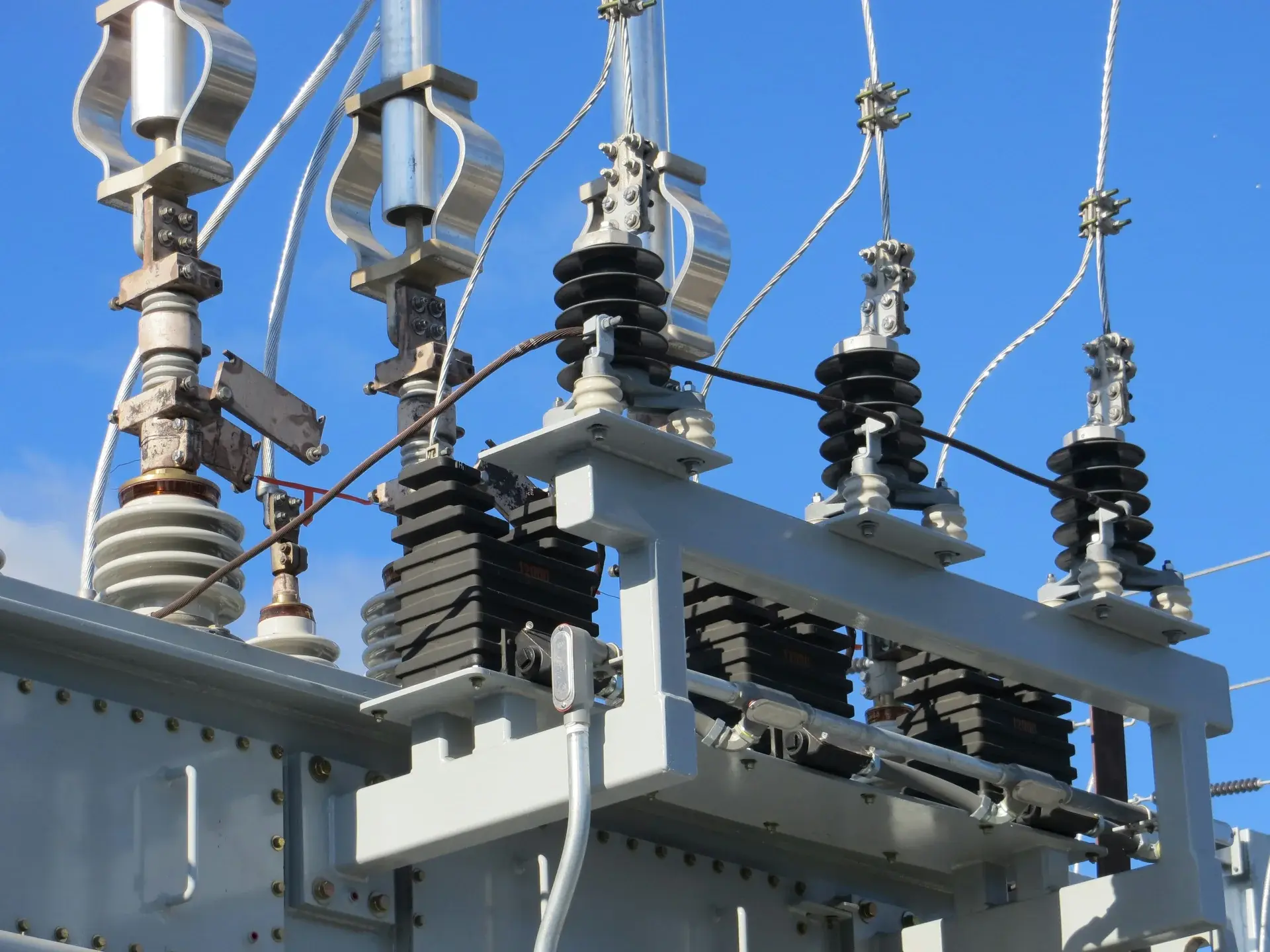 Close-up of high-voltage transformer insulators and switchgear at an electrical substation against a blue sky.