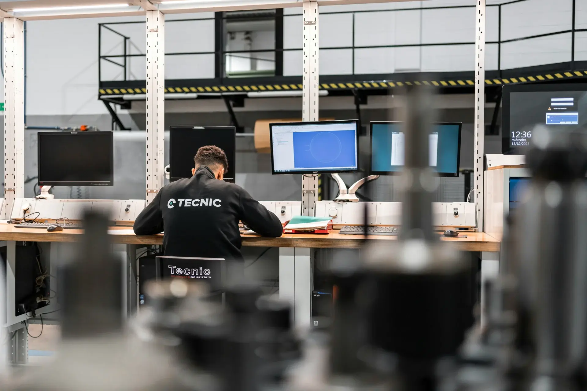 Industrial engineer working at a multi-monitor CAD workstation in a modern engineering design office.