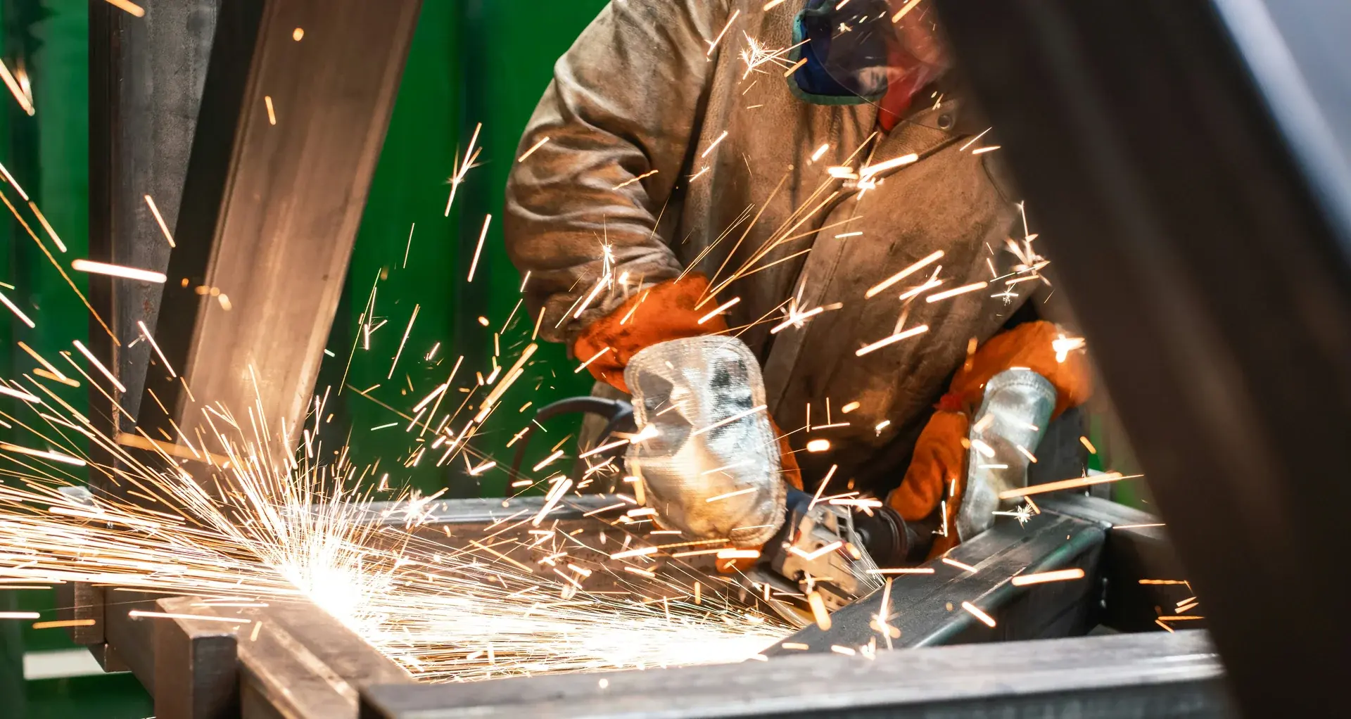 Metal worker using an angle grinder on steel beams.