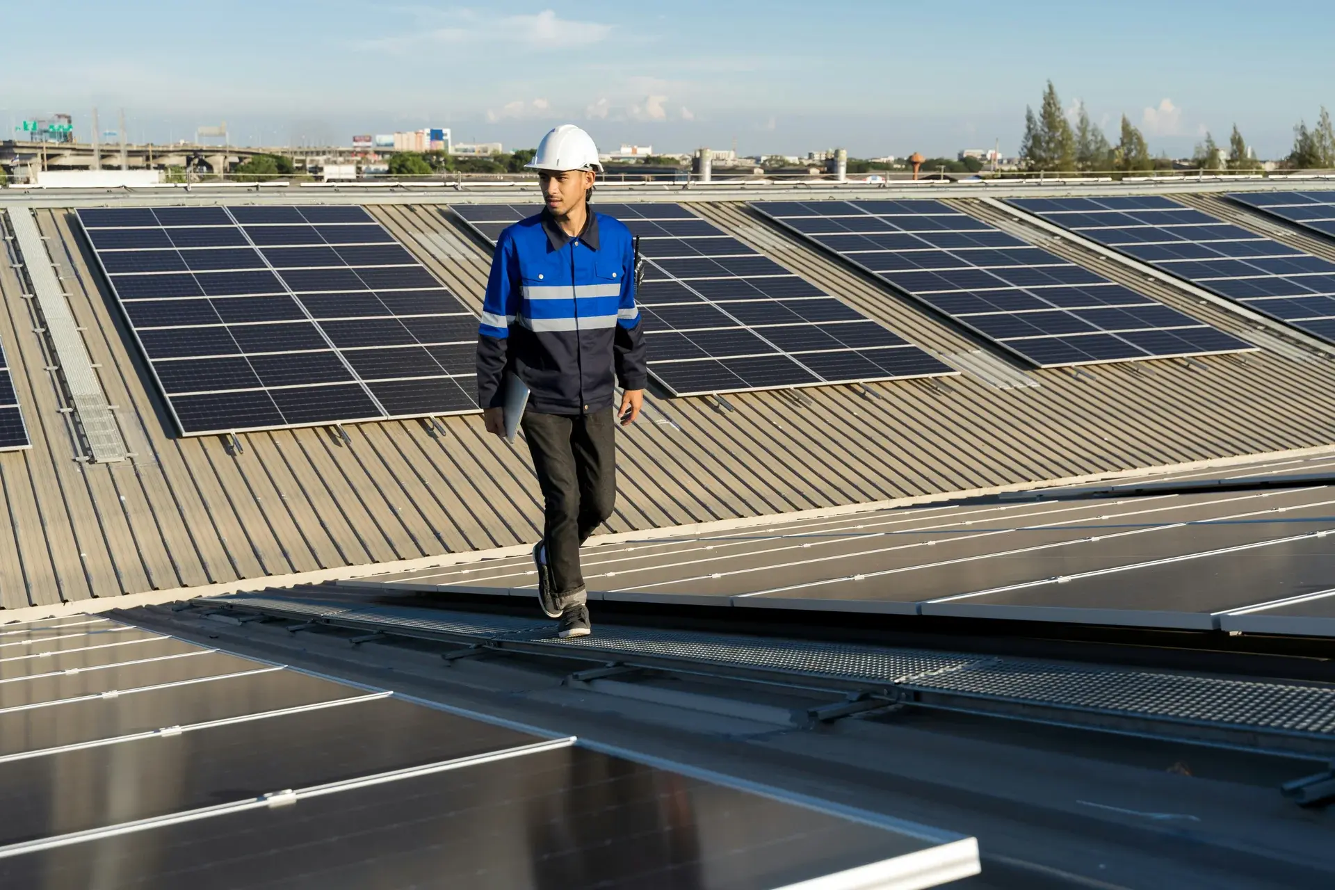 Solar engineer in hard hat and uniform walking between rows of photovoltaic panels on a commercial rooftop installation.