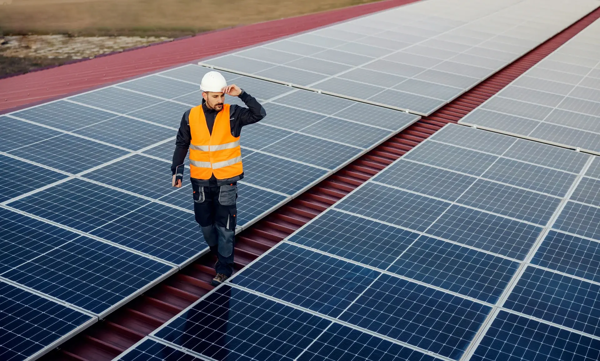 Solar technician in safety vest walking between rows of solar panels on a commercial rooftop installation.
