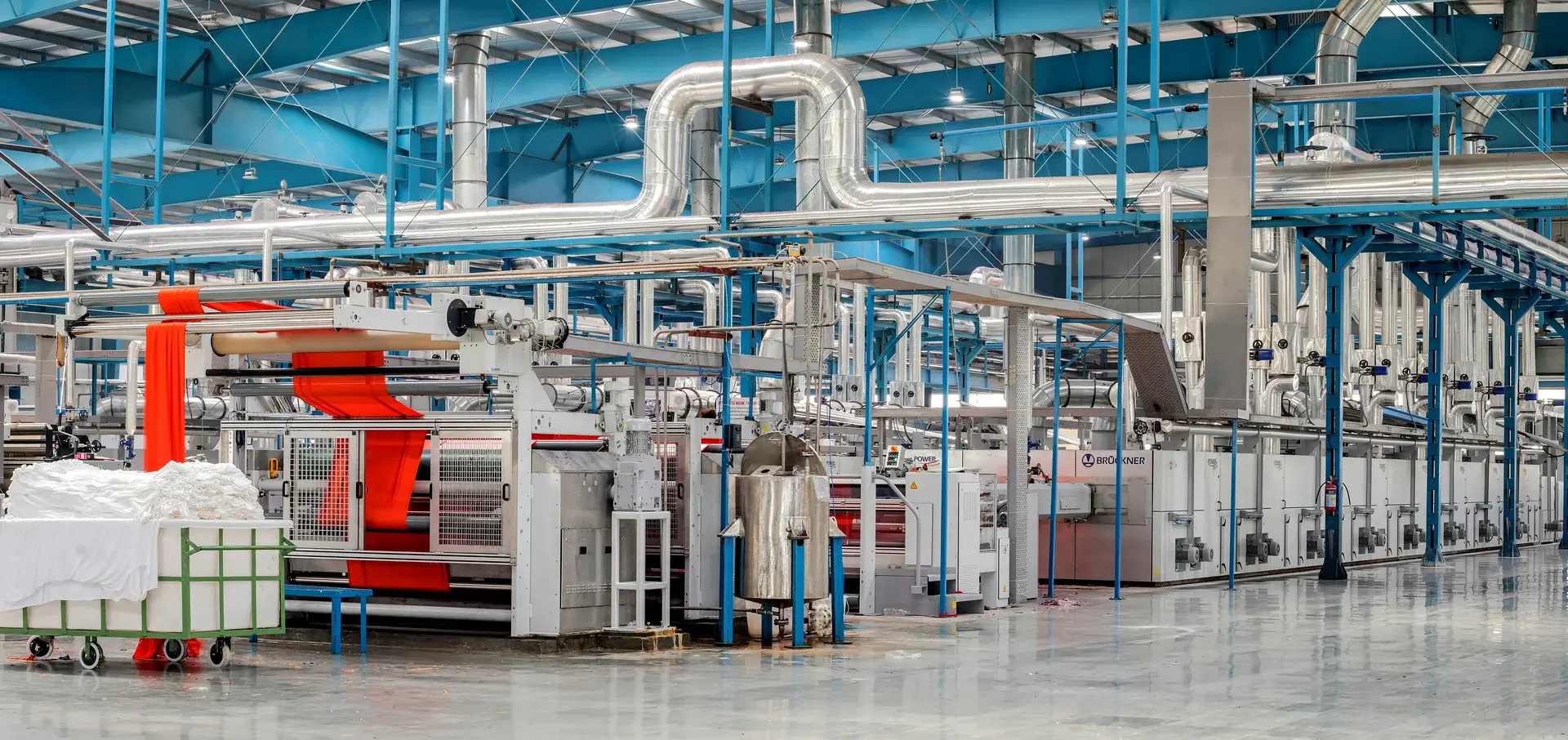 Wide view of an industrial textile manufacturing plant with a fabric dyeing and finishing production line processing red textile.