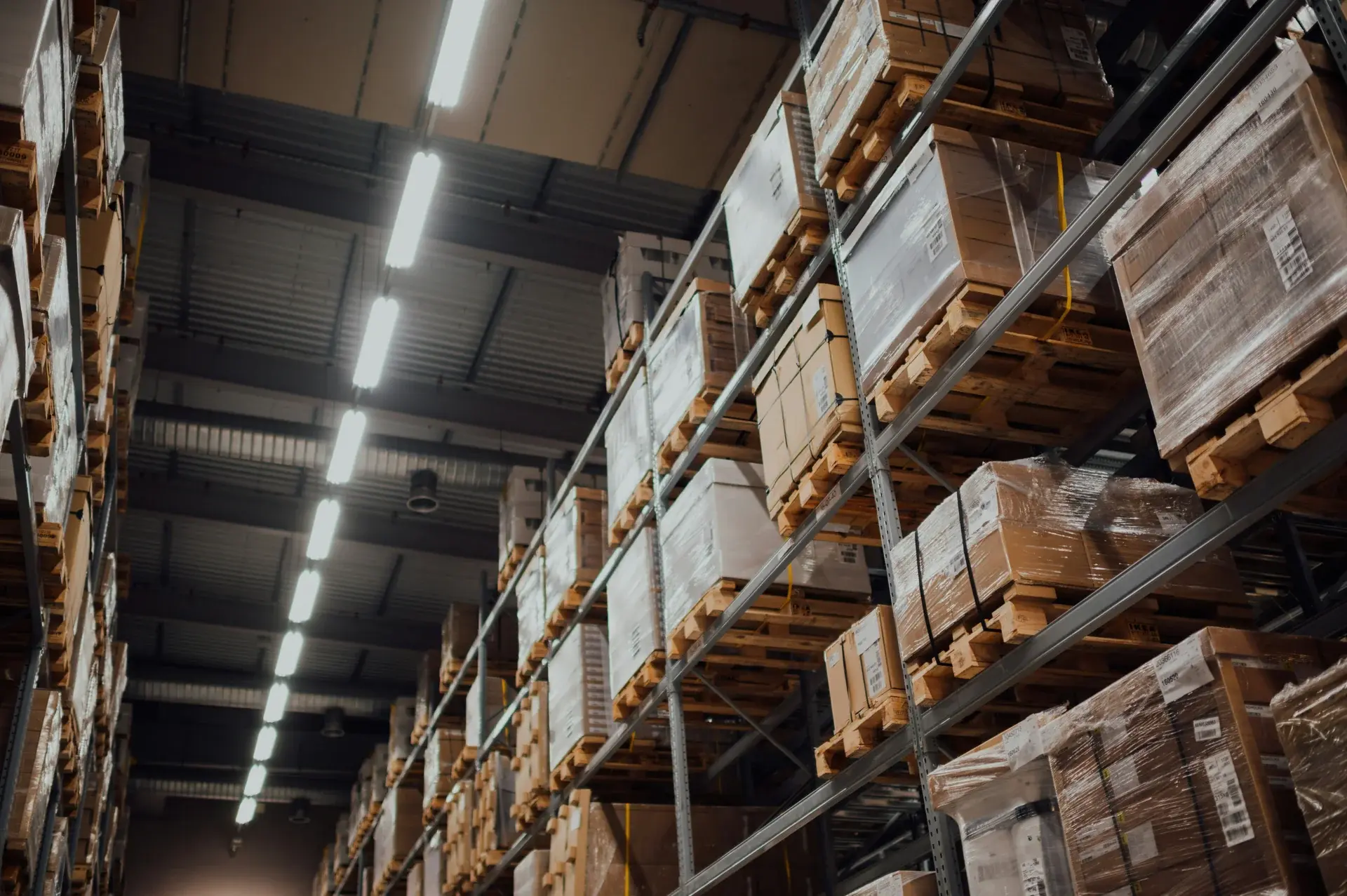 Tall warehouse pallet racking filled with boxed inventory under bright industrial lighting in a distribution center