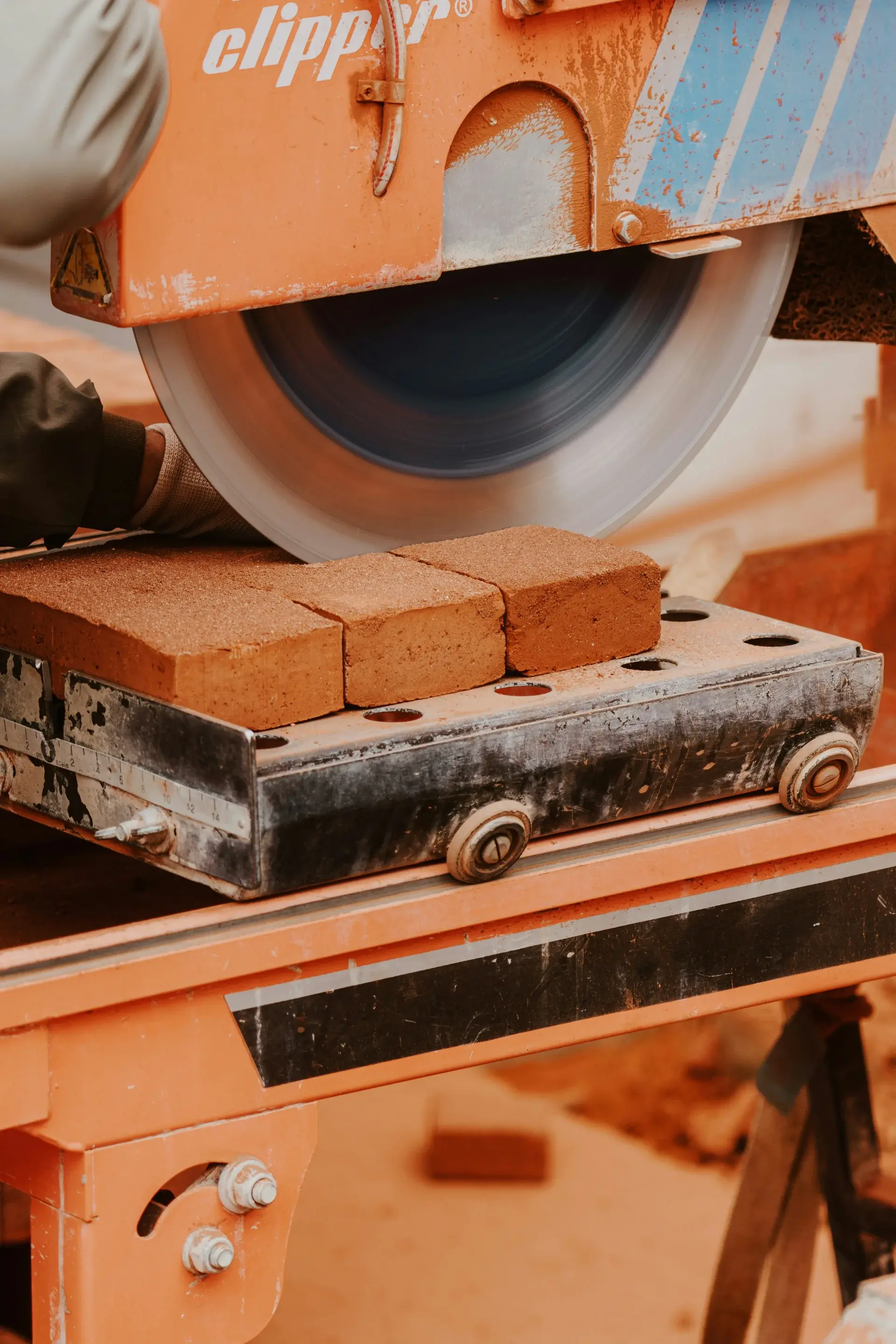 Masonry wet saw cutting through stacked clay bricks with a spinning diamond blade on a construction site.